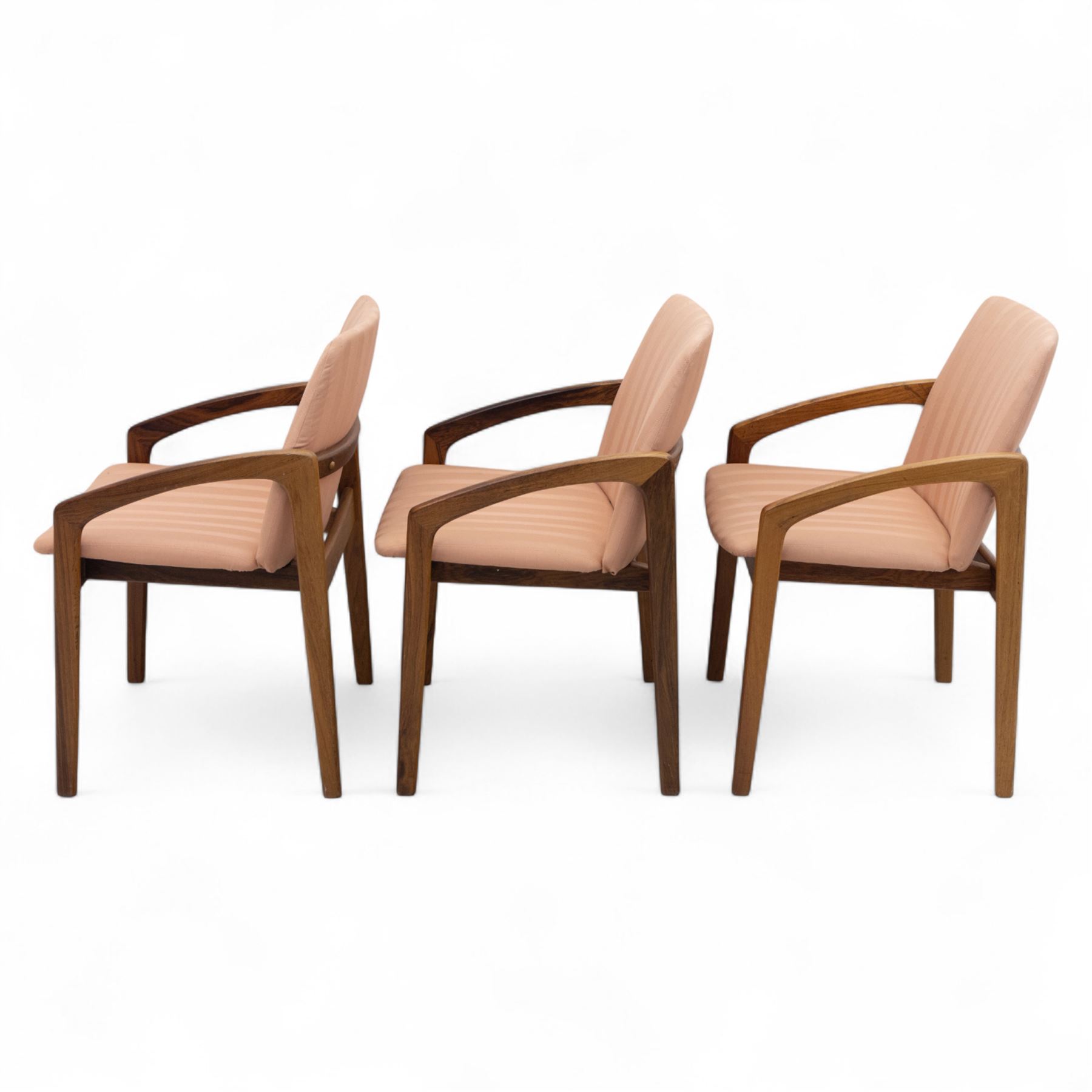 Mid-20th century Danish teak armchairs, each with curved open arms and upholstered seat and backrest in salmon pink striped fabric, raised on tapering legs