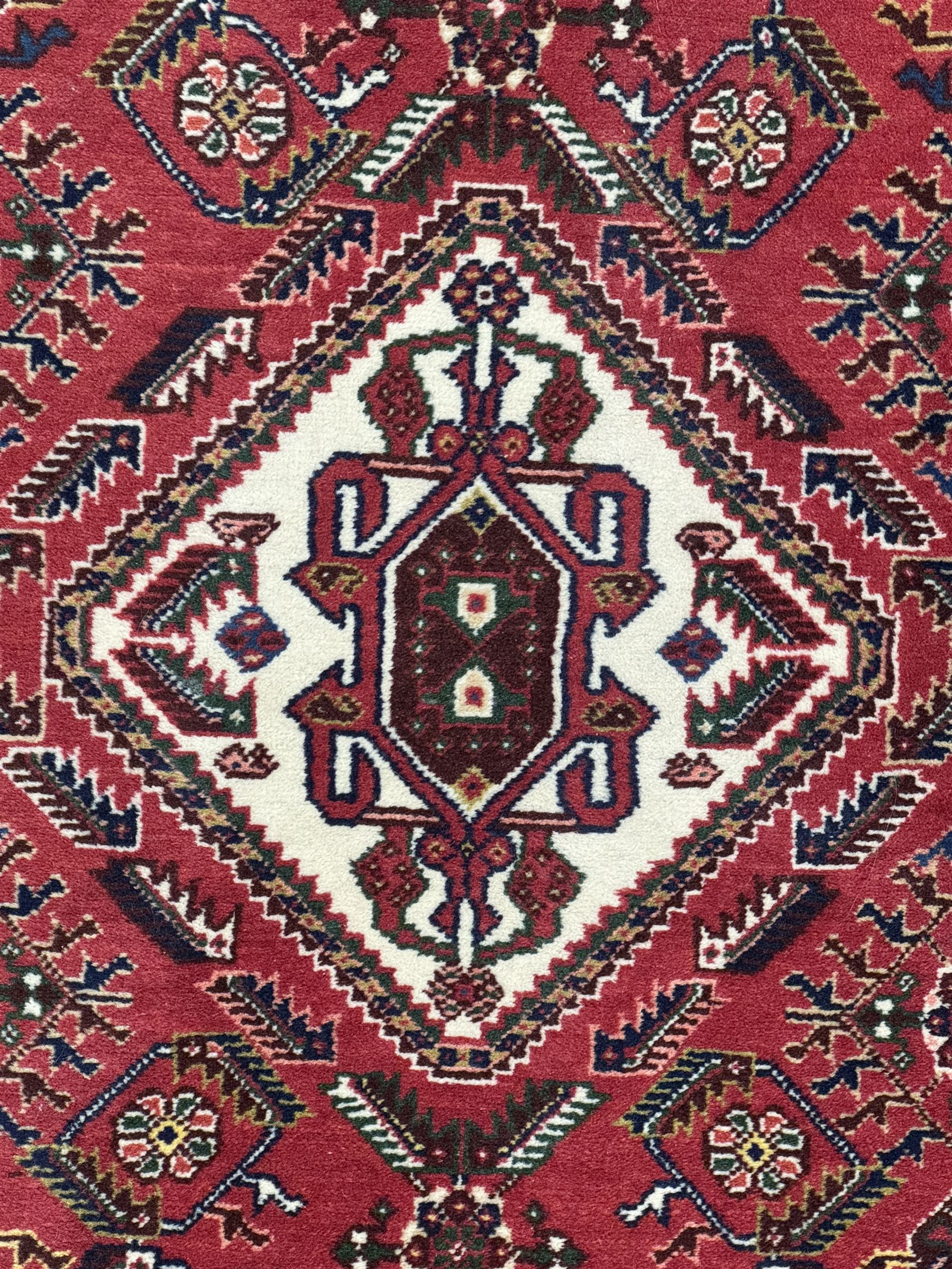 Persian Qashqai crimson ground runner, the central field decorated with three large geometric medallions with intricate angular and floral motifs, the indigo spandrels with complementary geometric designs, bordered by an ivory band with repeating floral patterns and angular vines