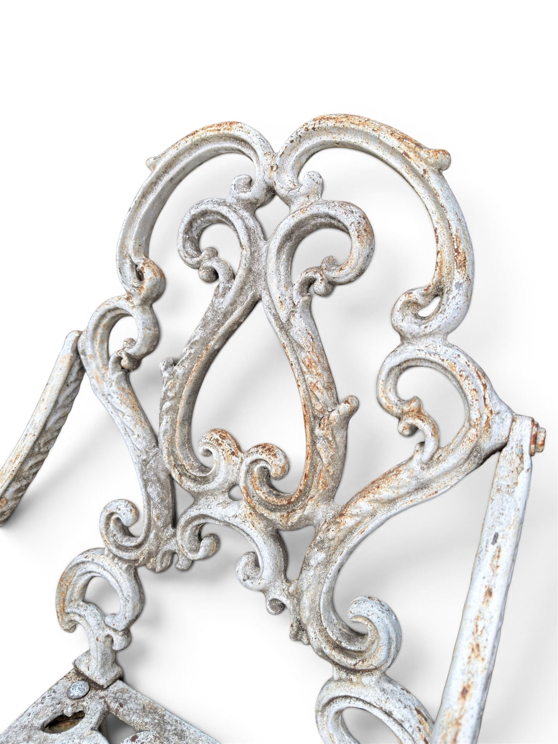 Pair of Victorian cast iron garden chairs, the ornate pierced back of scrolling foliate design, scrolling arm terminals over splayed supports formed of C and S-scrolls, in distressed white painted finish