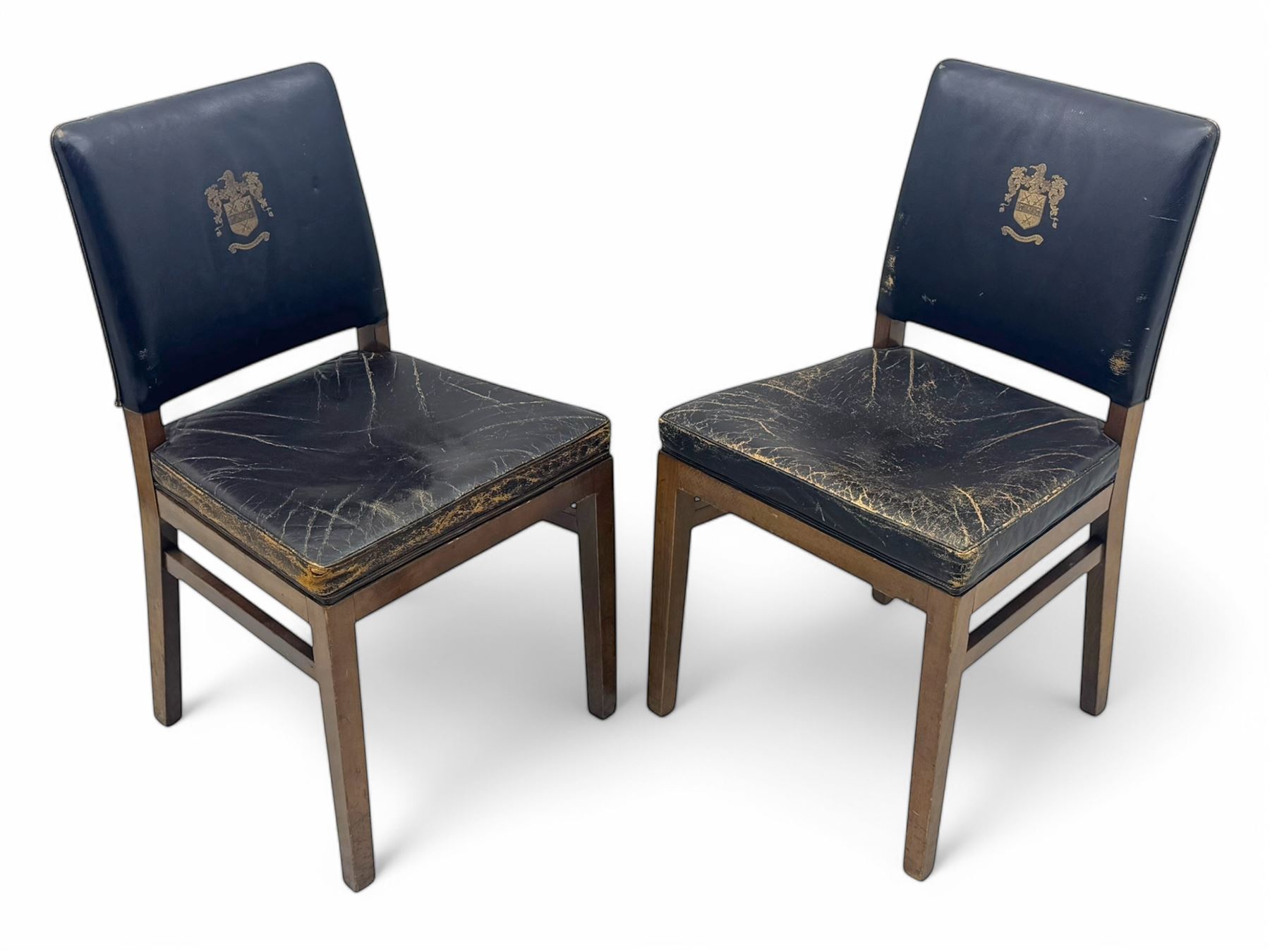 Pair of mid-20th century hardwood chairs associated with the Company of Cutlers in Hallamshire, Sheffield, each featuring a squared frame and black vinyl upholstery, the back emblazoned with the guild’s gilt coat of arms and motto “Pour Y Parvenir a Bonne Foi” (To Succeed through Honest Endeavour)