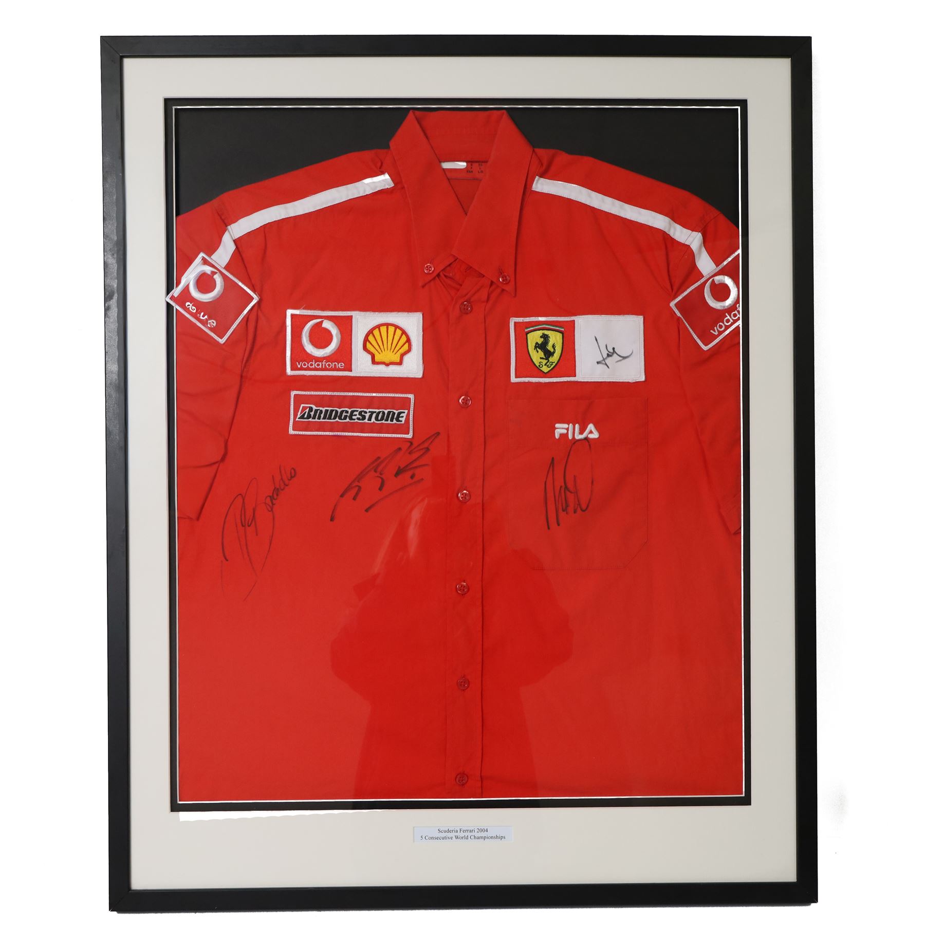 Scuderia Ferrari 2004 shirt, bearing four signatures including Michael Schumacher and Rubens Barrichello, to commemorate five consecutive World Championship wins, in glazed frame, frame H85cm