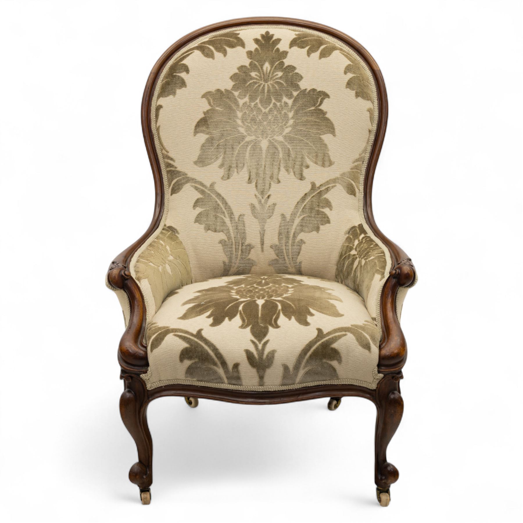 Victorian mahogany framed spoon back armchair, the shaped and padded back over serpentine seat upholstered in a floral damask pattern fabric within a moulded frame carved with scrolled arms, raised upon cabriole front legs with scroll feet on porcelain castors 