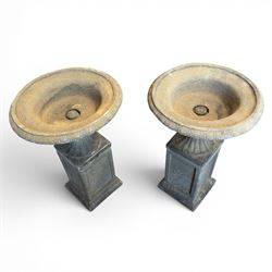 Pair of cast stone garden urns of kylix form on pedestals, the broad egg-and-dart moulded rim over a shallow gadrooned underbelly, with waisted tapering base, raised on matching plinth bases with faux panelled facia