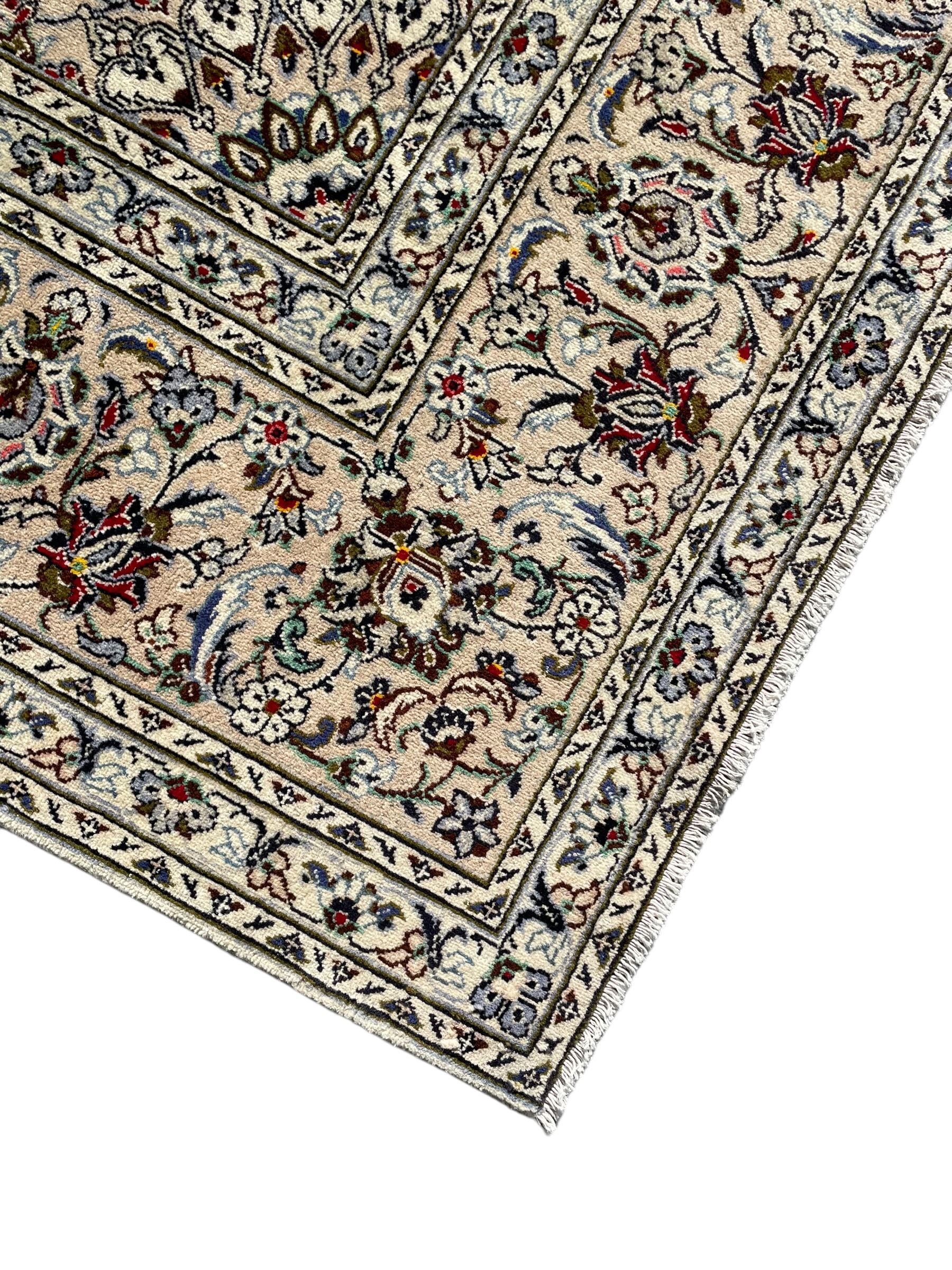 Persian Kashan ivory ground carpet, central rosette medallion with projecting palmettes, densely decorated field depicting trailing leafy branches and stylised plant motifs, the border with similar scrolling pattern, within floral pattern guard stripes 