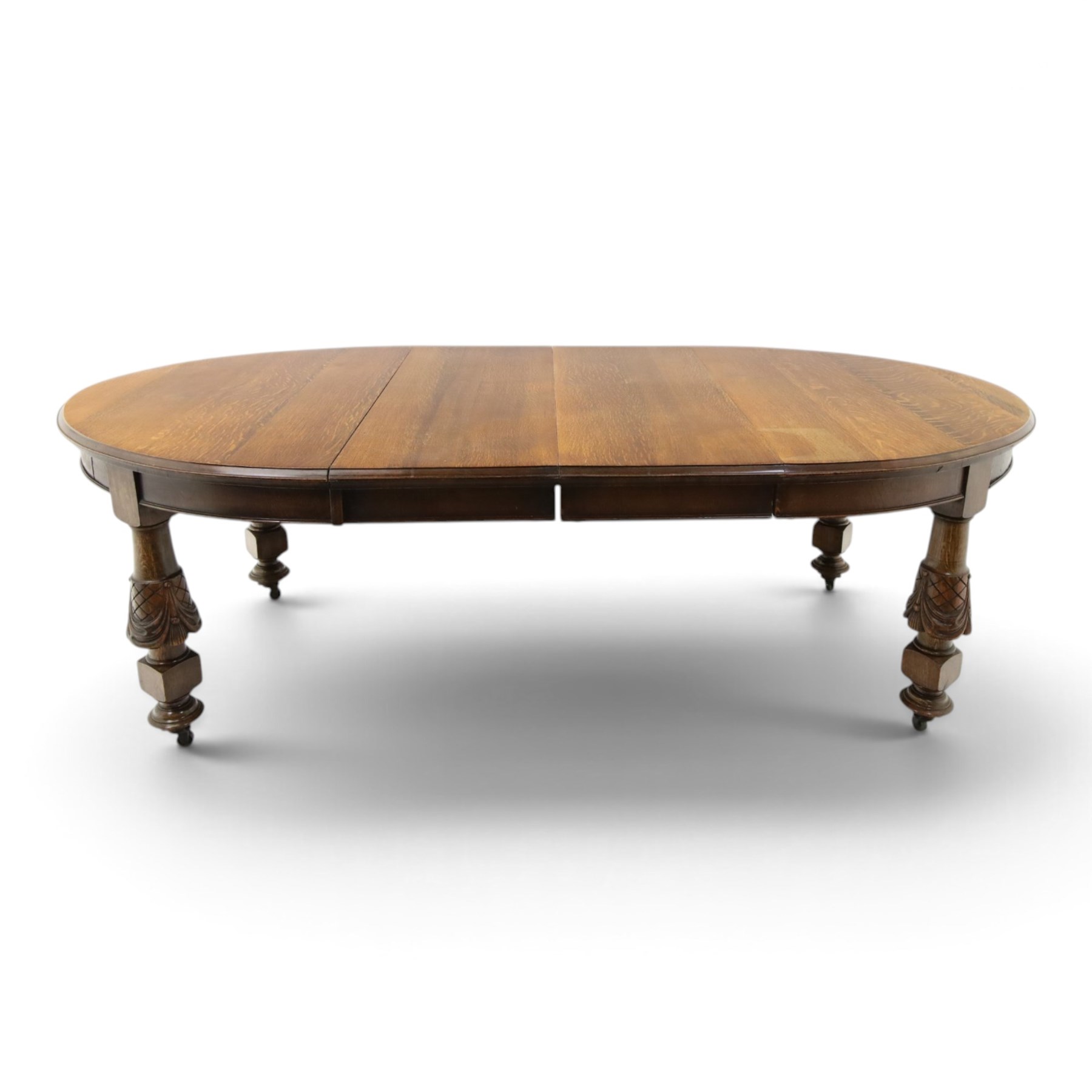 Late 19th century French oak extending dining table, oval top with moulded edge and plain frieze, raised on four ornate carved supports decorate with carved latticework and large festoons with tassels, on turned feet, with two additional leaves