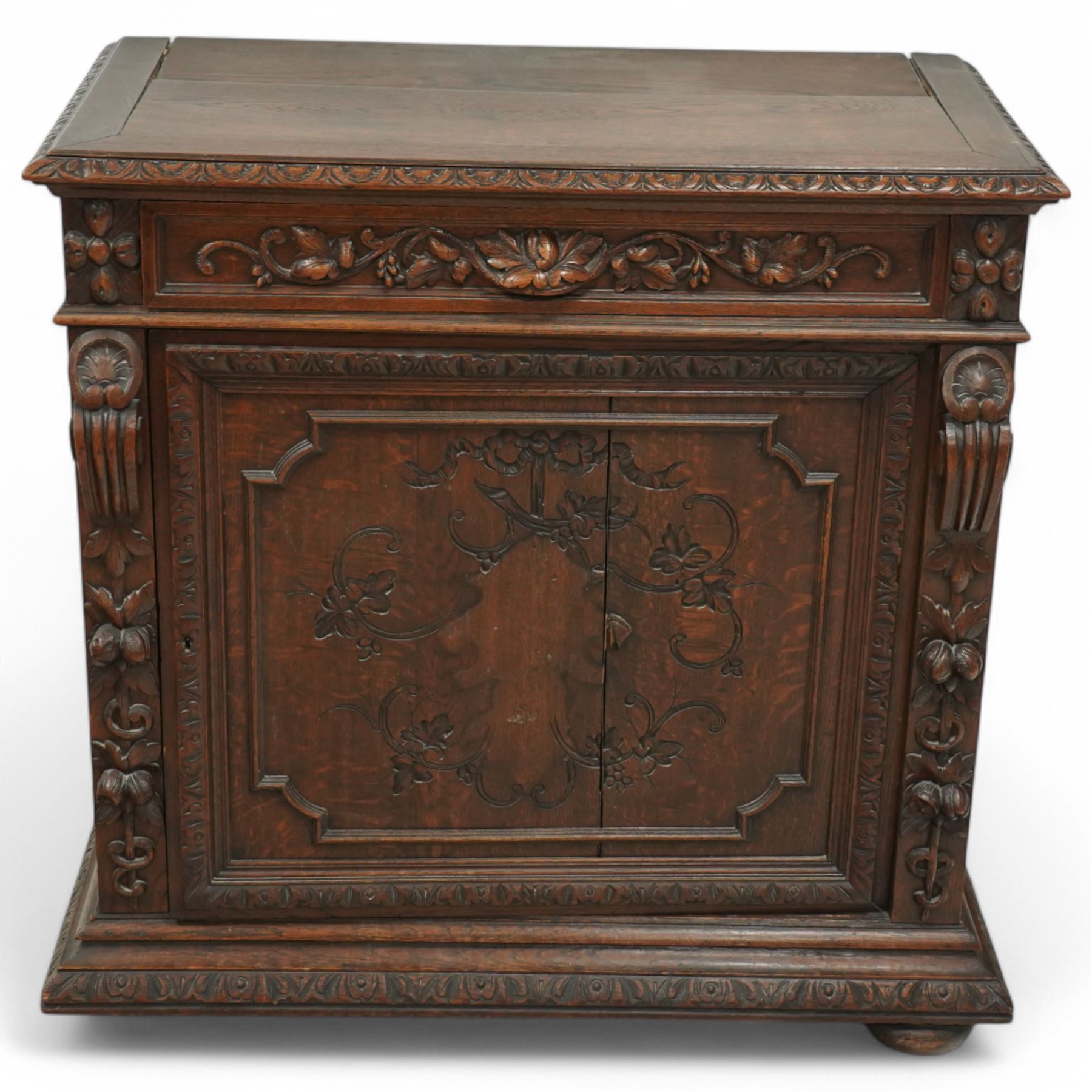 19th-century heavily carved oak baroque style cupboard with vine and floral carved frieze drawer above panelled cupboard door with floral carved appliqué (detached) flanked by symmetrically carved scroll and vine decorated sides, on bun feet 