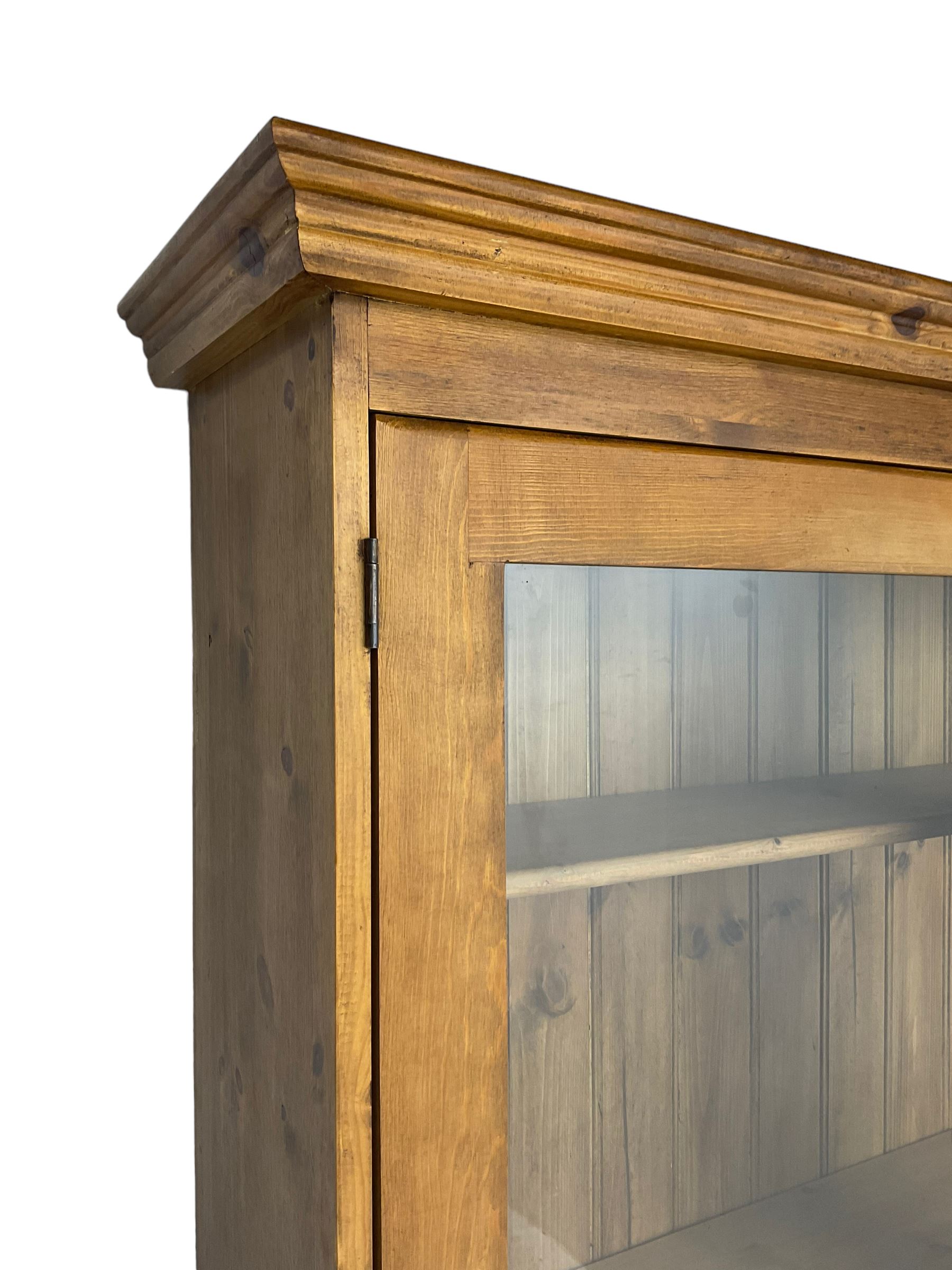 Large pine bookcase on cupboard, the upper section enclosed by two glazed door, the lower section fitted with two drawers and double cupboard, on plinth base