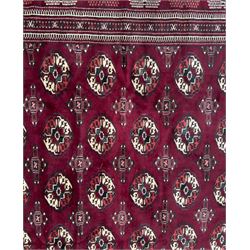 Northeastern Persian Yamut  hand-knotted carpet, the rich burgundy field with repeating rows of stepped gul motifs in cream and black, enclosed by multiple linear and geometric borders with hooked motifs and diamond medallions