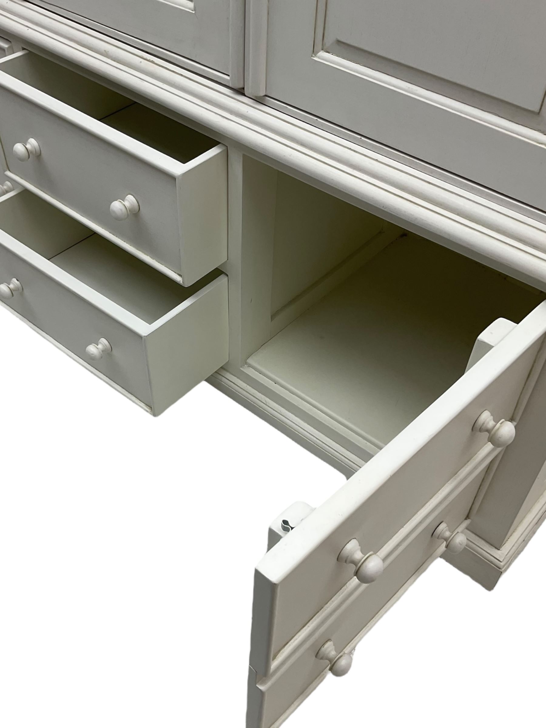 White painted triple wardrobe, projecting moulded cornice over three panelled doors, the interior fitted with hanging rails, four drawers and hinged cupboard to base, on bracket feet