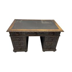 Late 19th century Gothic revival carved oak twin pedestal desk, rectangular top with inset writing surface and carved edges, central frieze drawer flanked by eight drawers, all with green man carved handles and extending trailing foliate scrolling, the pedestals with panelled sides and back, on plinth base with compressed bun feet 