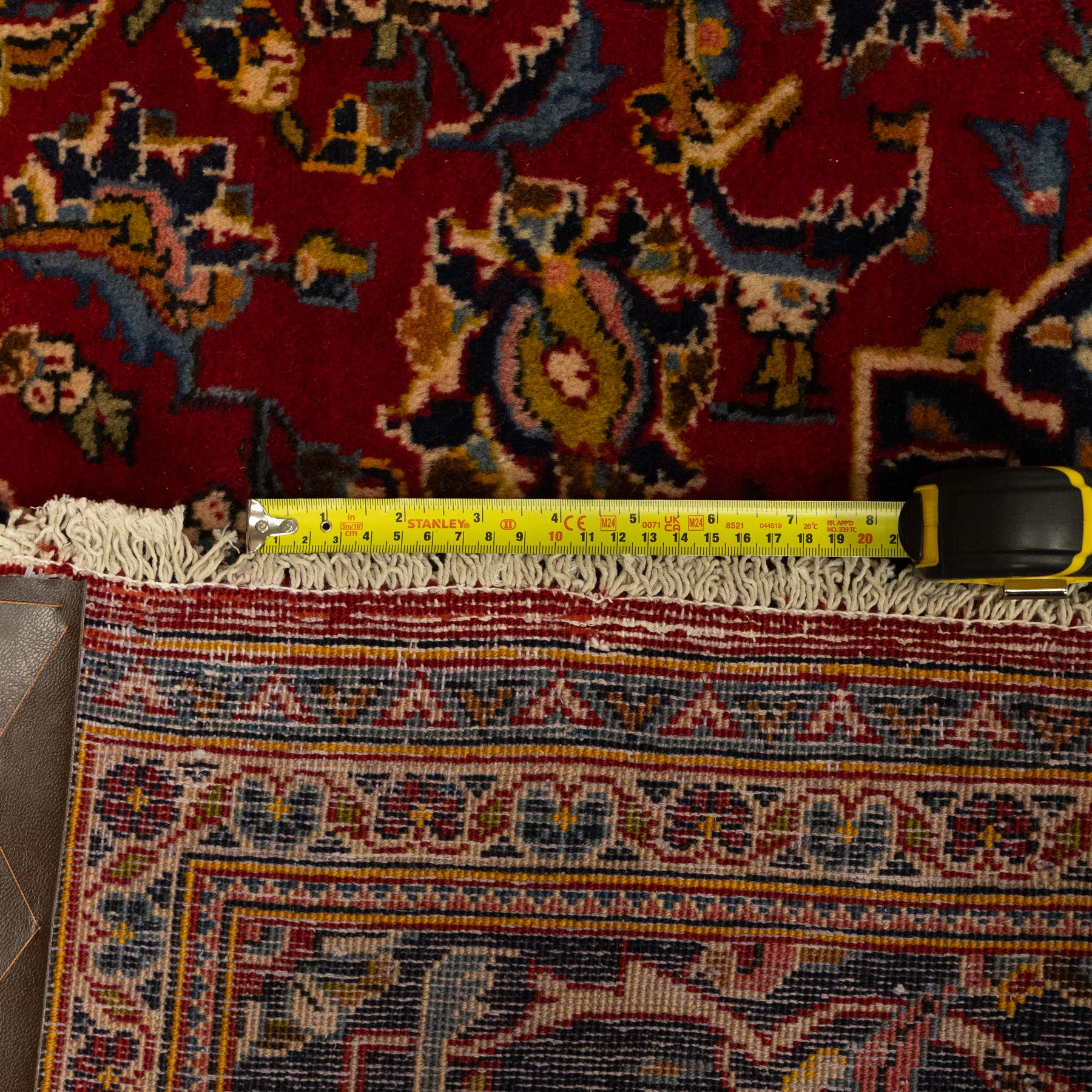 Central Persian Kashan hand-knotted carpet, crimson red field with a central shaped palmette medallion with pendants, filled with dense scrolling and floral motifs, enclosed by a navy blue border decorated with palmettes and meandering vine scrolls, flanked by multiple guard stripes, with cotton fringe ends 