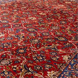 Central Persian Markazi Mahal hand-knotted carpet, terracotta red field, with an all-over scrolling vine design issuing with palmettes, rosettes, and serrated leaves, linked by ivory vinery, deep cobalt blue main border with floral ornamentation, flanked  by multiple guard stripes of repeating geometric motifs, with cotton fringe ends