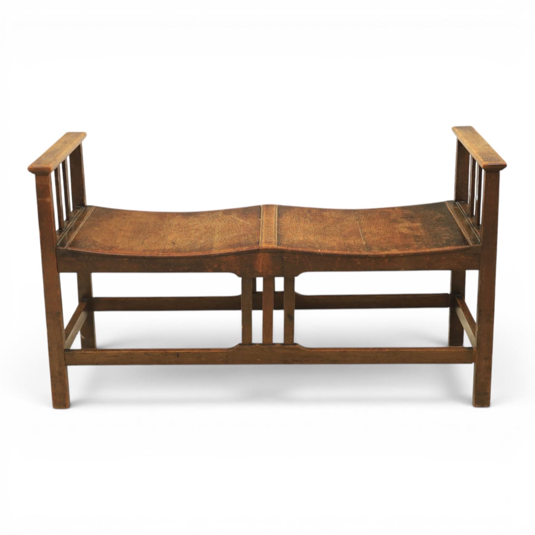 Arts and Crafts oak window bench, with flat armrests flanking two dished seats, raised on square supports united by stretchers