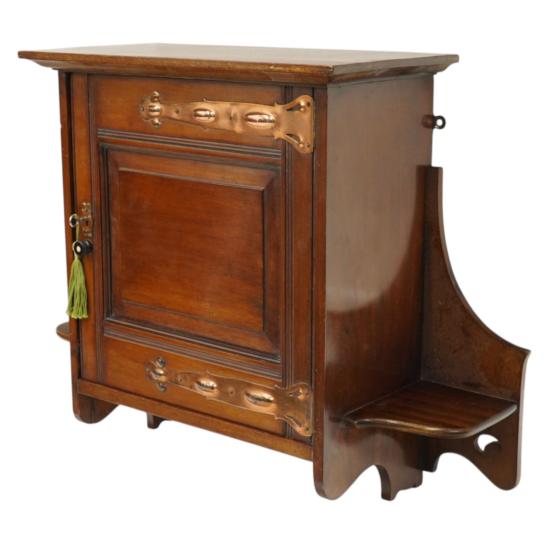 Small Arts & Crafts mahogany wall cupboard, single panelled door enclosing shelf, flanked by two shelves with pierced brackets, with shaped copper fittings and escutcheon 