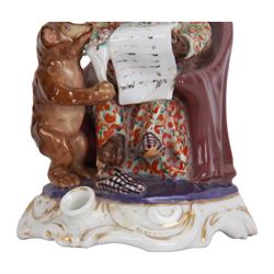 Mid 19th century French porcelain inkwell, possibly Jacob Petit, circa 1884, modelled as a anthropomorphic bear seated within an armchair, wearing cap, gown and slippers, reading a letter to a small cub holding a bunch of flowers, upon a shaped and scrolling base, impressed and incised marks beneath, H19cm
