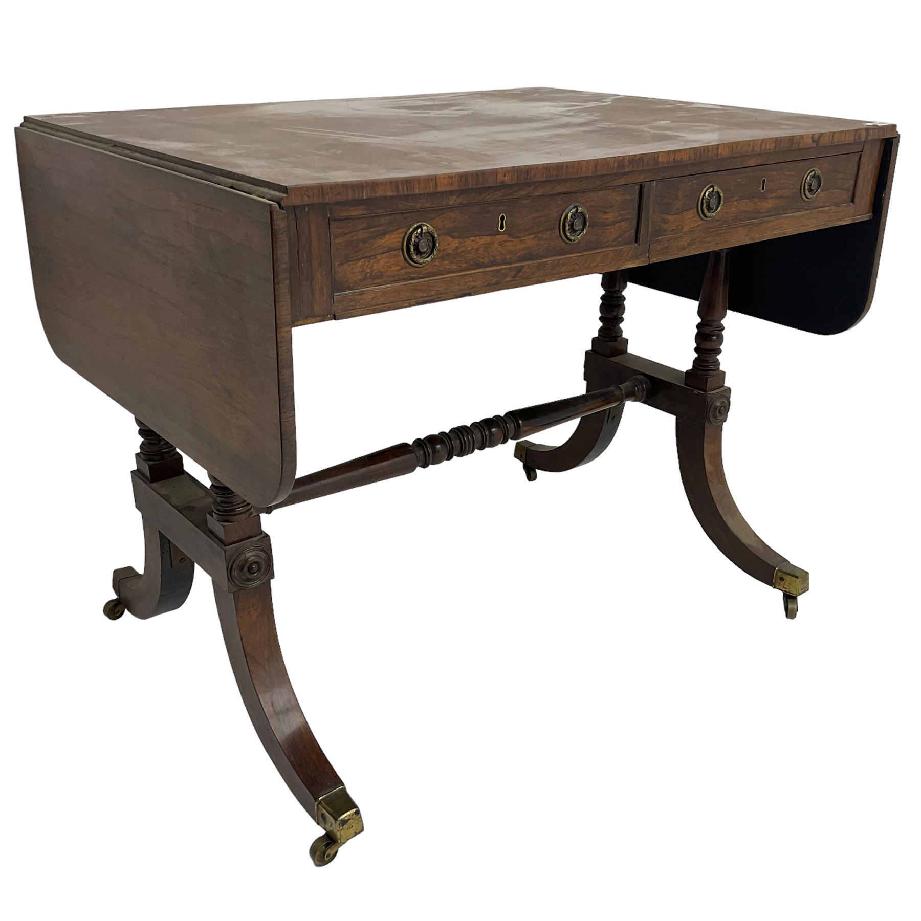 Regency rosewood sofa table, drop leaf rectangular top with rounded corners, fitted with two drawers and two opposing false drawers, raised on dual turned columns terminating in splayed feet united by turned stretcher, on brass cups and castors