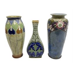 Two Royal Doulton stoneware vases, the first example with tubelined floral decoration, the second with Art Nouveau decoration, together Doulton Lambeth vase of flattened form with foliate decoration on a green ground, all with impressed mark beneath, tallest example H26cm
