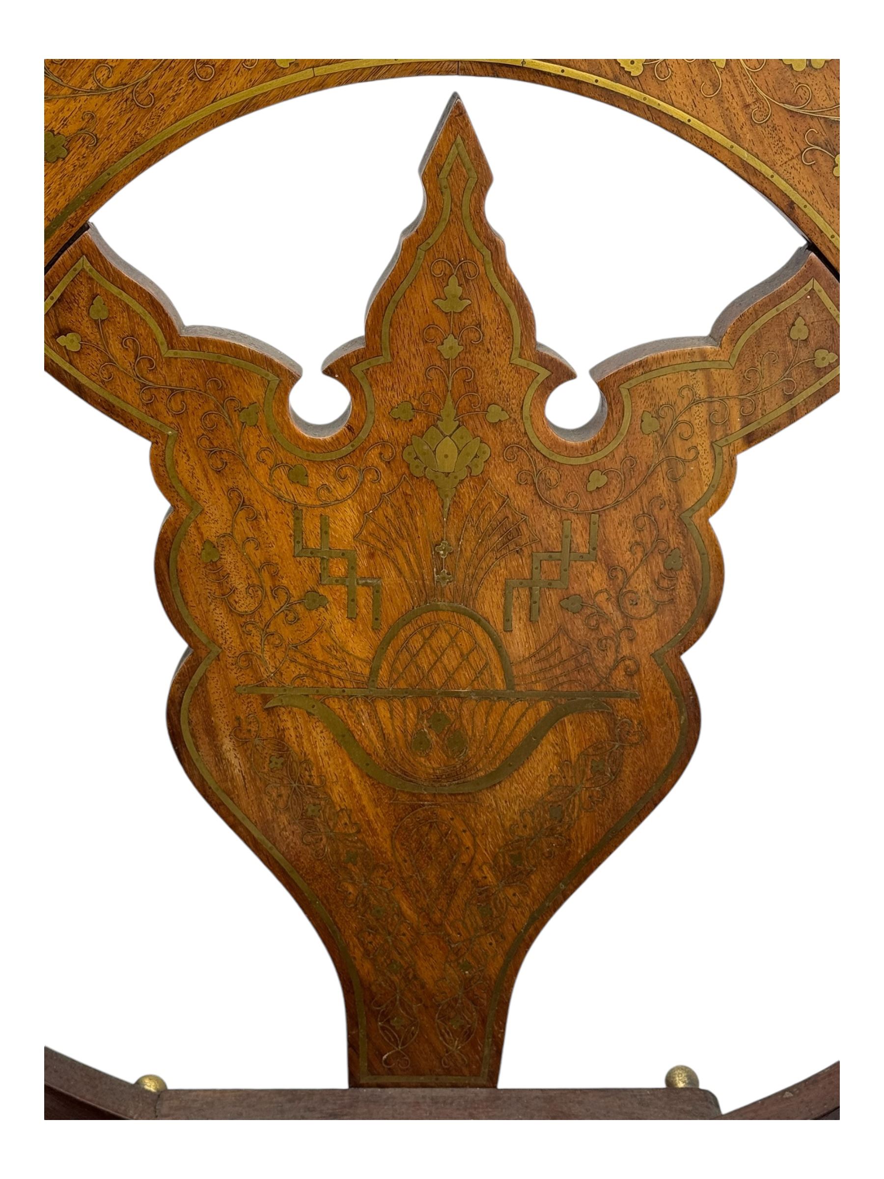 Late 20th century brass inlaid hardwood throne chair, curved X-frame form, raised shaped back inlaid with trailing leafy branches and flower heads, on sledge feet 