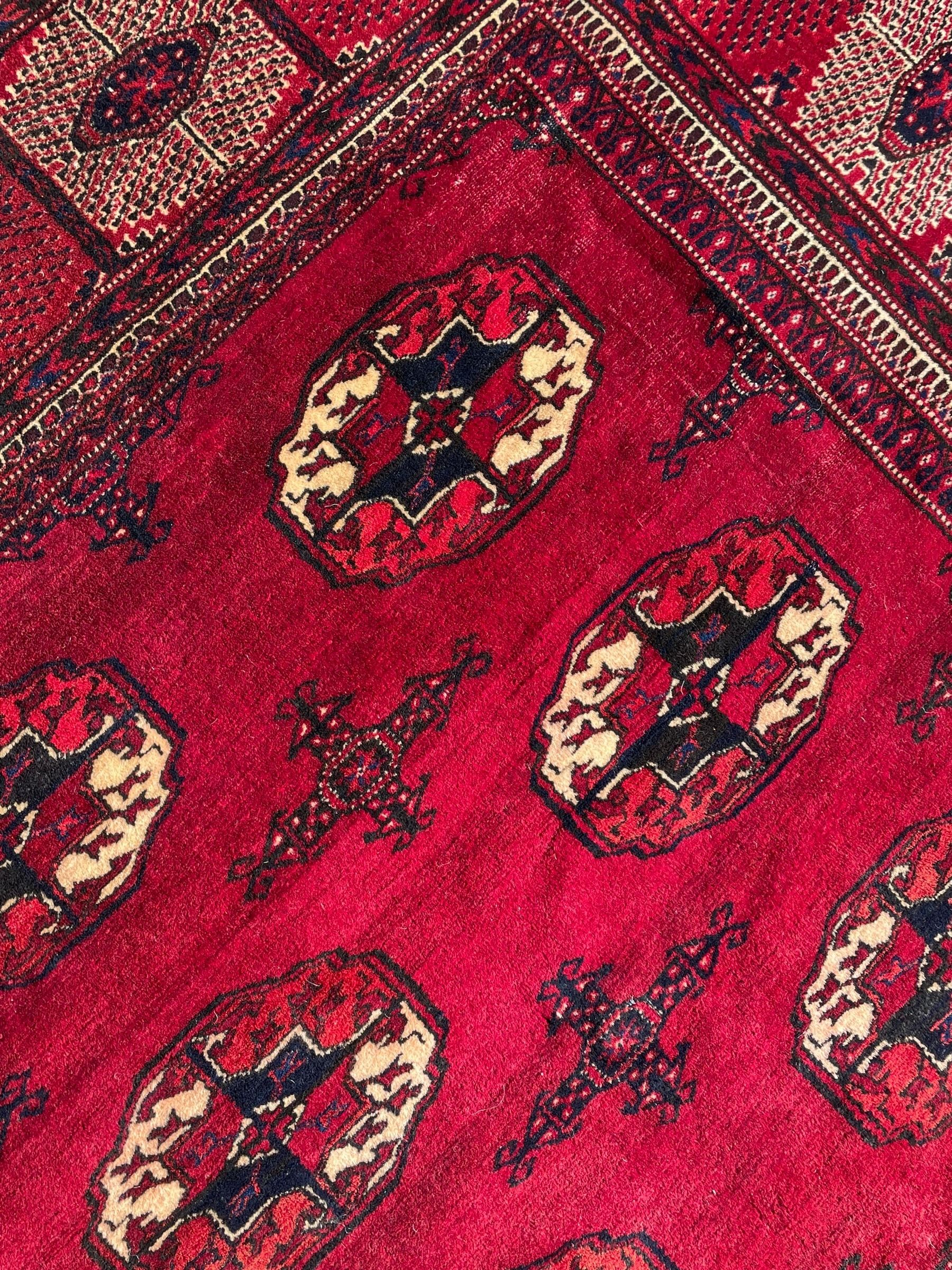 Afghan Bokhara red ground carpet, the field decorated with four rows of Gul motifs interspersed with Hac motifs, the border with lattice pattern panels within small geometric guard stripes, geometric patterned end panels