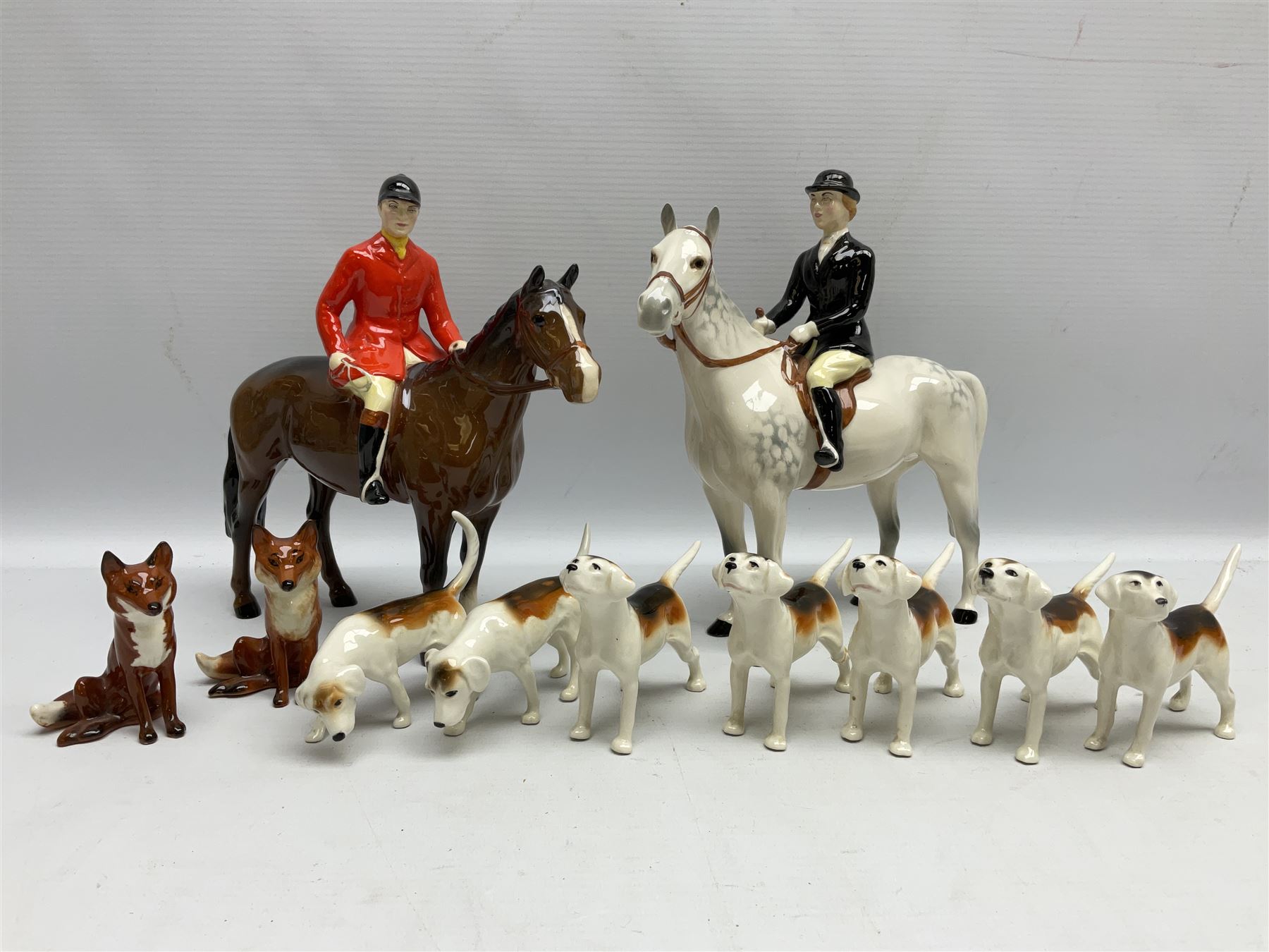 Beswick hunting group, comprising huntswoman on grey horse no 1730, huntsman on brown horse no 1501, two seated fox figures no 1748 and seven fox hounds, all with printed marks beneath (11)