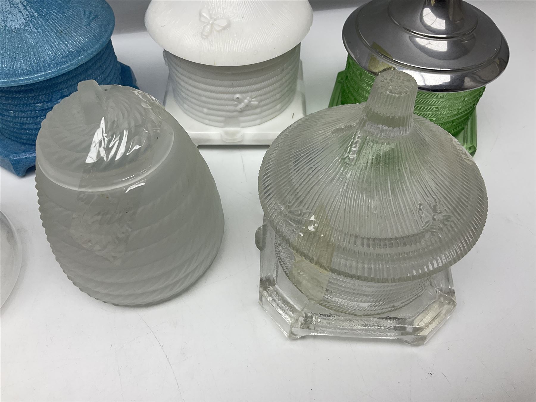 Collection of glass beehive honey pots, to include a blue slag example, milk glass, pink, green, etc together with four white metal examples (16) 