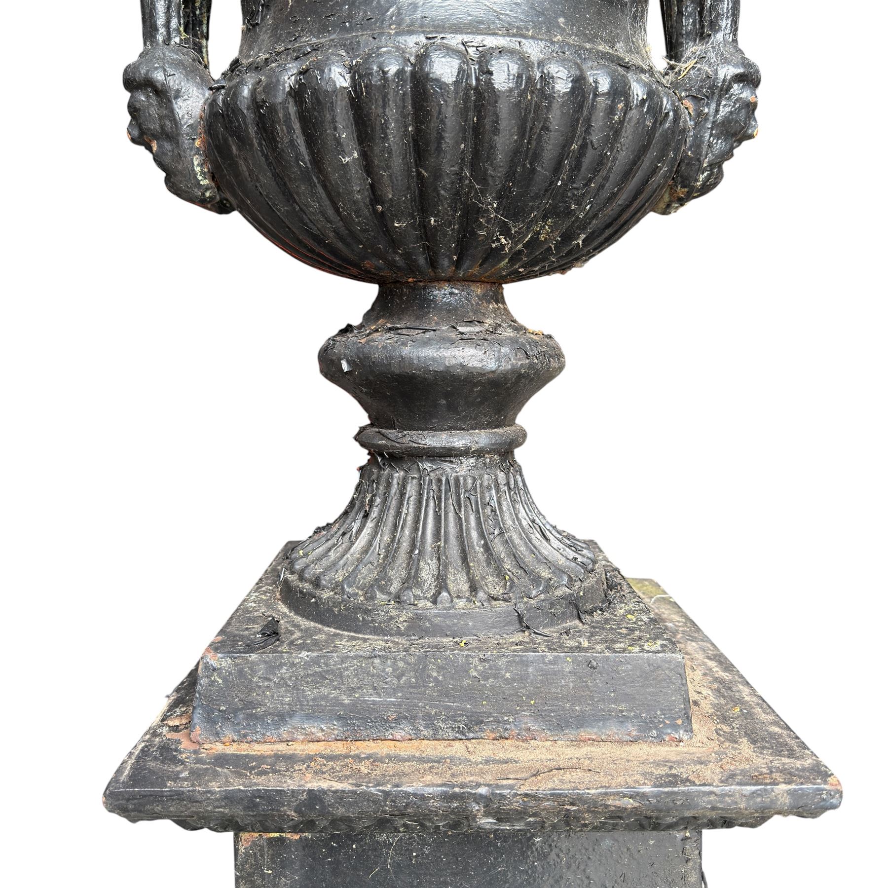 Pair of Victorian cast iron campana form garden urns, the gadrooned flared edge over a scrolling acanthus relief body, with twin male mask handles to each side, over a lobed underbelly with fluted socle, the rectangular pedestals with relief floral garlands and stepped base, in rustic black-painted finish, planted