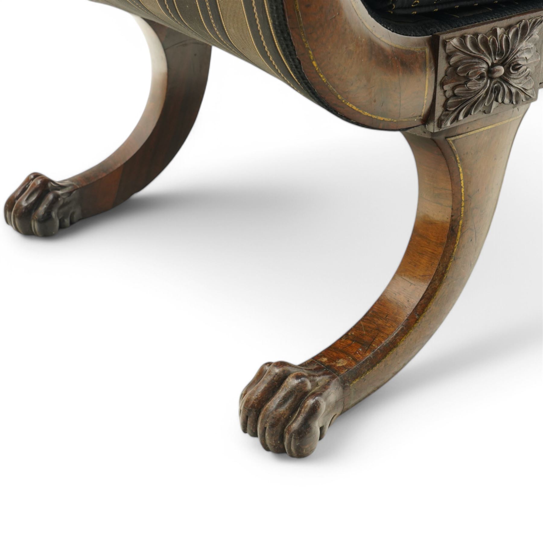 Regency brass inlaid rosewood chaise lounge or settee, shaped back over rolled head and foot, upholstered in black and gold striped fabric with rectangular squab cushion and bolster cushion, the rolled terminals carved with acanthus leaf roundels, lower rectangular foliate carved panels, on out splayed supports with paw carved feet 