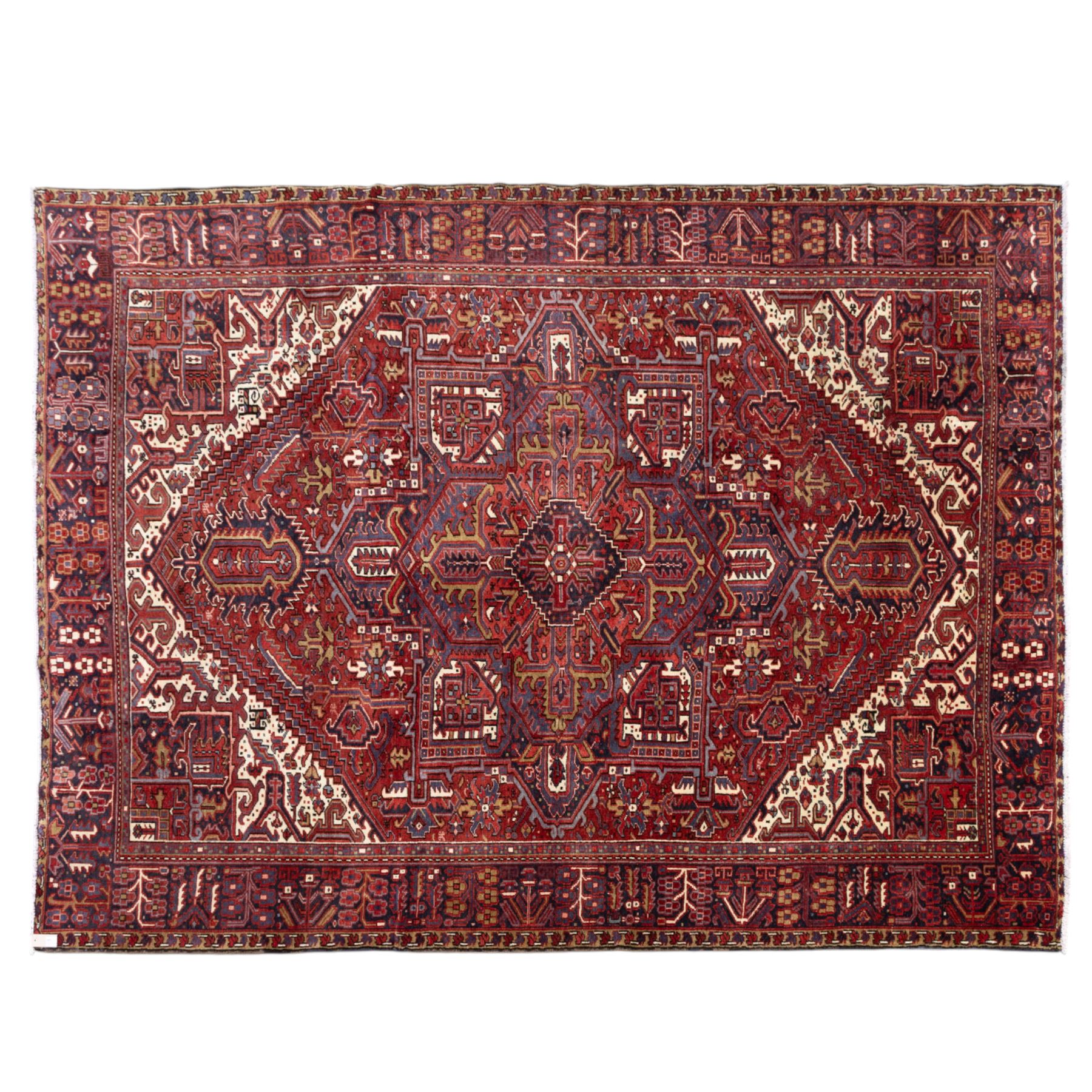 North West Persian Heriz hand-knotted carpet, madder red field with central bold angular steeped medallion with serrated outlines, flanked by stylized palmettes, hooked leaves and geometric motifs, spandrels similarly decorated within a wide geometric border and multiple guard borders in tones of madder red, indigo blue, ivory and olive green, with cotton fringe ends  