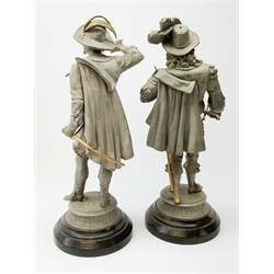 Pair of stripped 19th century spelter figures of cavaliers with brass detailing, each standing with sword drawn and wearing a plumed hat and cape, on ebonised metal stepped base H52cm