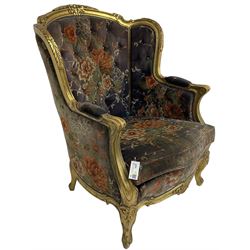 Pair of Louis XVI design gilt framed wingback armchairs, cresting rail carved and moulded with foliate decoration and C-scrolls, upholstered in buttoned floral patterned mauve velvet with loose seat cushion, scallop carved apron over cabriole supports