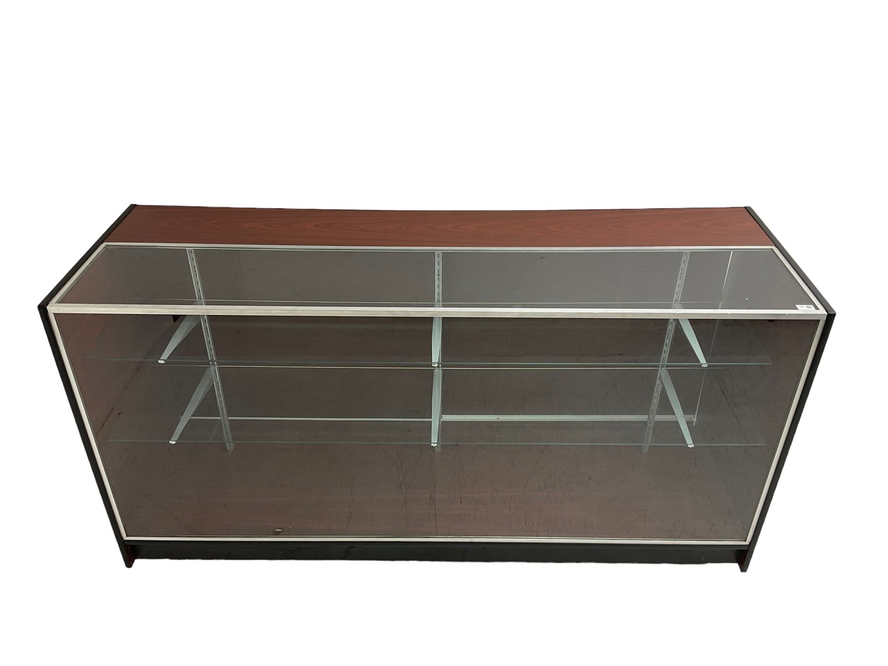 Shop display cabinet counter, glazed front and top, with mahogany laminate sides and back, enclosing two long adjustable shelves, fitted with two sliding cupboard doors to the rear, on castors