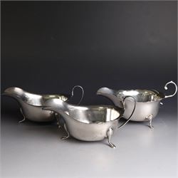 Three silver sauce boats, comprising pair of 1930s silver sauce boats, of typical form with shaped rim, scroll handle and upon three pad feet, hallmarked Viner's Ltd, Sheffield 1932 and a similar 1920s example with flying C scroll handle and upon three paw feet, hallmarked James Deakin & Sons, Sheffield 1923, tallest including handle H7.5cm