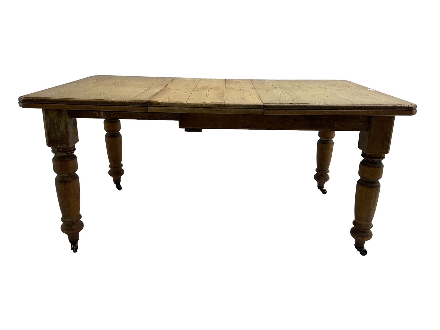 Late Victorian pine extending dining table, rectangular moulded top with canted corners and additional leaf, on turned supports with brass castors 