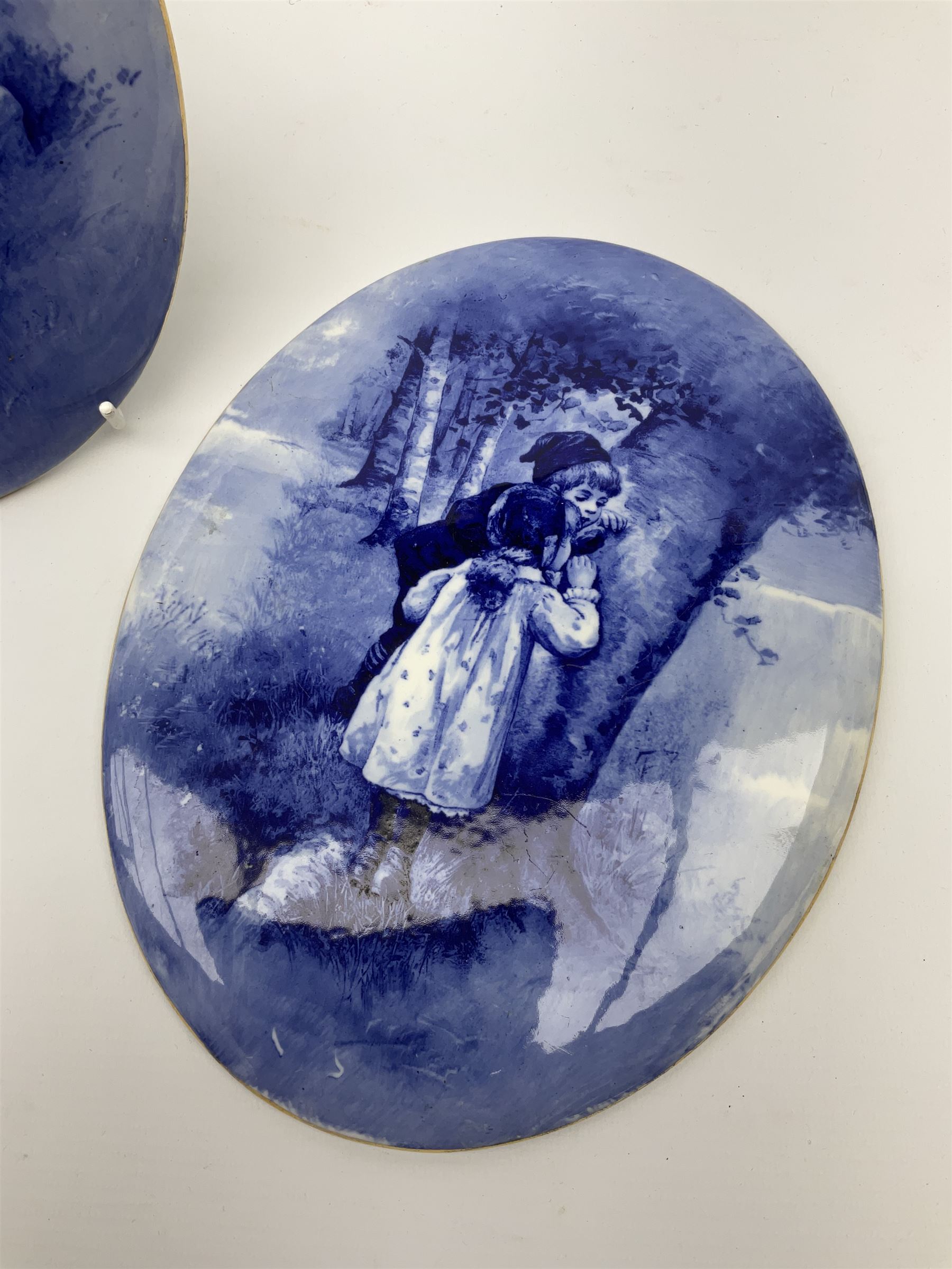 A pair of Royal Doulton blue and white plaques, of oval form decorated with children, one example with printed mark beneath, H24.5cm L19.5cm. 