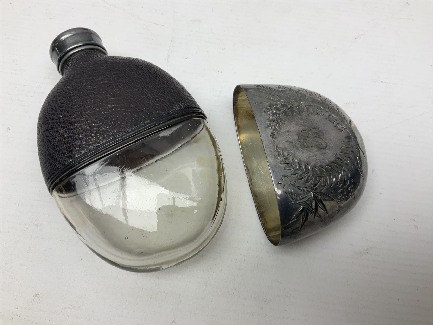 Silver plated glass and pressed leather hip flask, with swivel cap and removable cup, together with a similar oval example, engraved with wreath and initial B, tallest H16.5cm