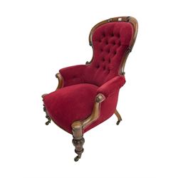 Victorian mahogany armchair, scroll carved cresting rail and uprights, upholstered in buttoned red fabric, turned and lobe carved front feet with brass castors