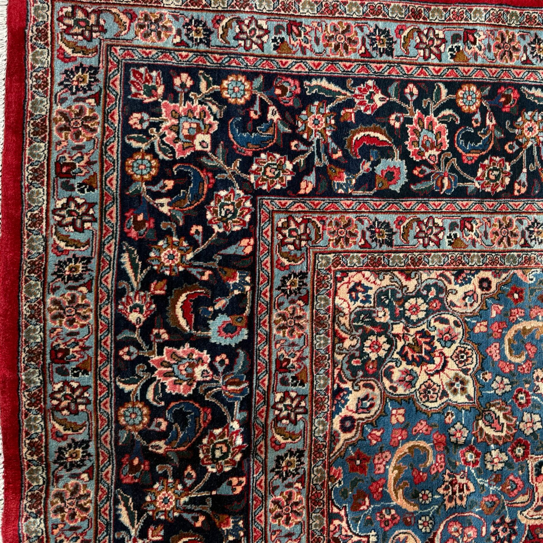 Meshed Persian rug, red, indigo, and teal background with repeating floral vine around a symmetrical floral medallion with bold palmettes, central ivory radiating floral centrepiece, and spandrels, indigo and teal border of delicate scrolling palmette and leafy floral vines