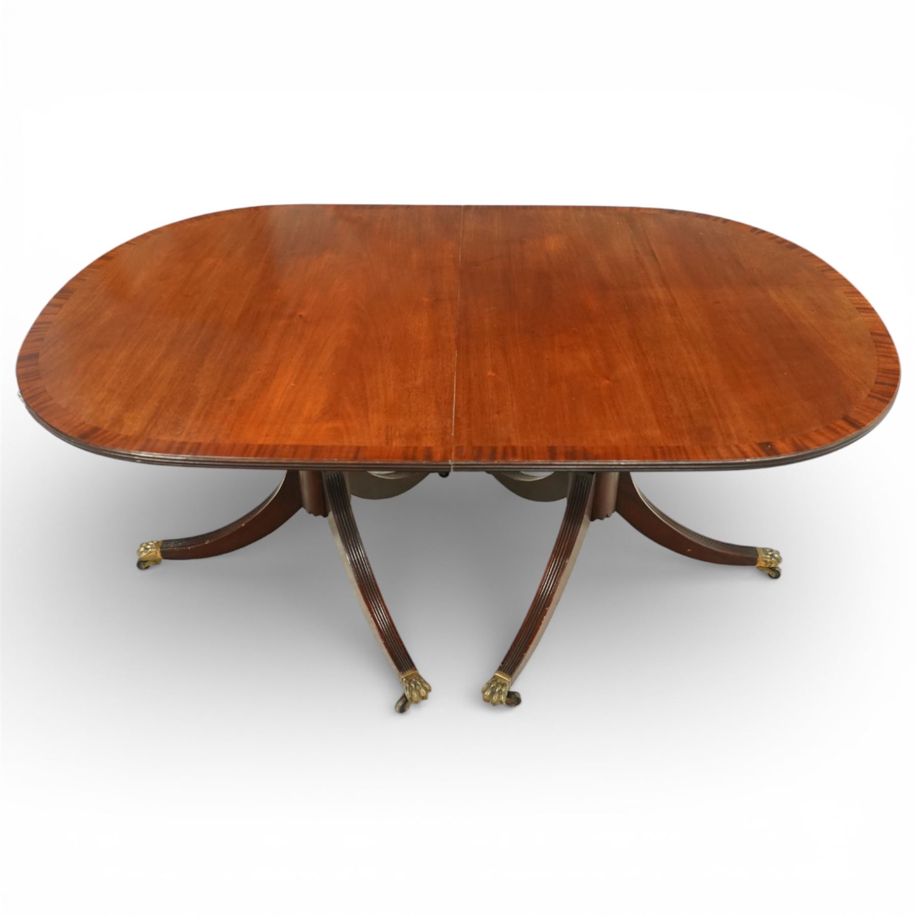 Arthur Brett & Sons - Regency design mahogany extending dining table and eight chairs, the oval top with rounded ends and two extension leaves, raised on twin pedestal supports with swept legs terminating in brass caps and castors, accompanied by a set of eight chairs comprising six single chairs and a pair of carvers, the chairs with curved backs and horizontal splat rails, upholstered seats, sabre legs and scrolling arms to the carvers
(Extends to 252cm)
(Chairs H 86cm, W 52cm)