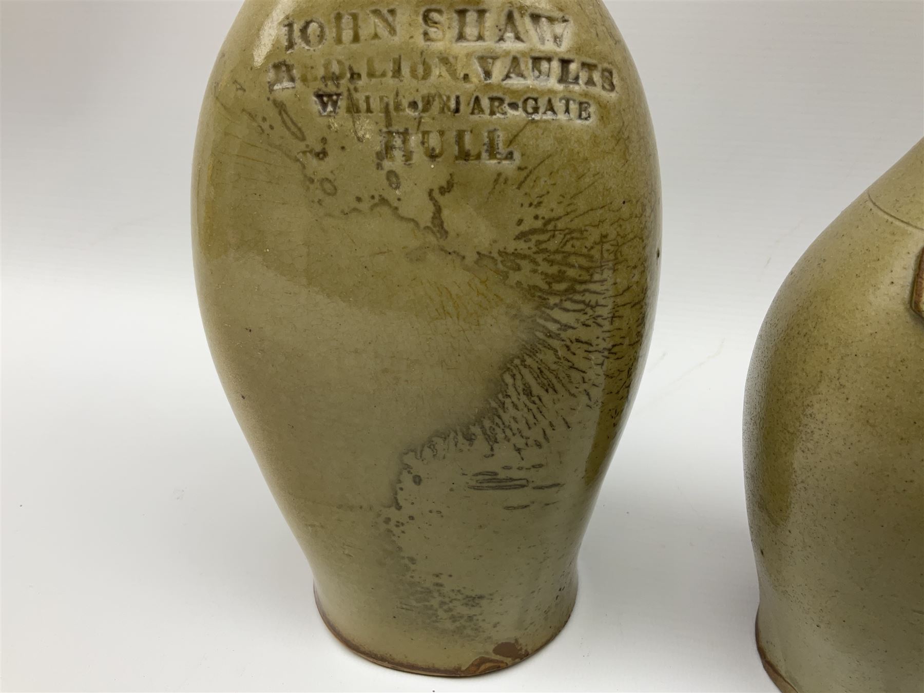  19th century salt glazed stoneware gin bottle impressed John Shaw, Red Lion Vaults, Whitefriargate, Hull of bulbous oval form H27cm and another with impressed label for J. Christie Mytongate Hull (2)  