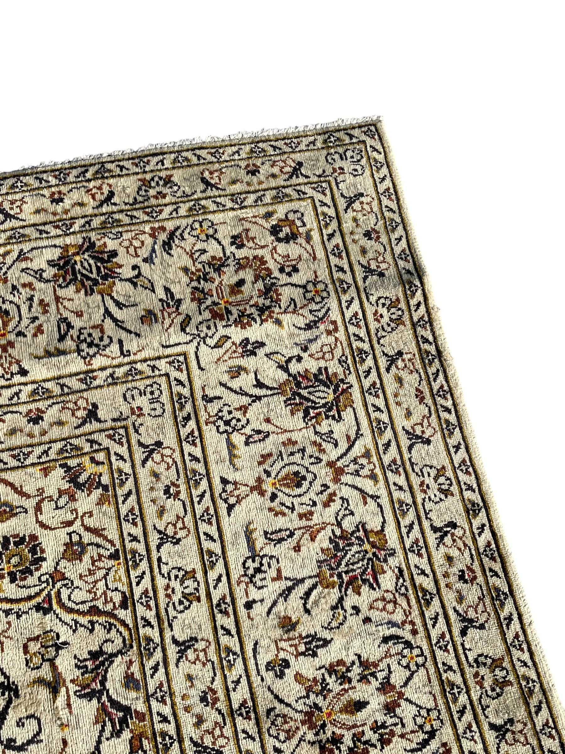 Persian Kashan ivory ground carpet, central medallion decorated with sixteen arranged palmette motifs, within a field decorated with swirling leafy branches and stylised plant motifs, the main border decorated with matching swirling pattern, within floral pattern guard stripes 
