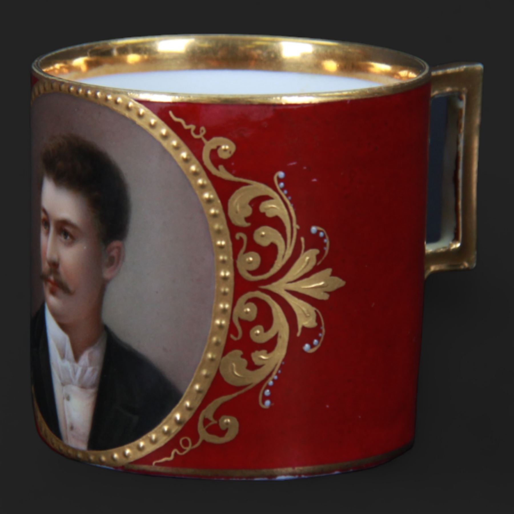 Late 19th century Vienna style coffee can and saucer, the cup with oval panel containing hand painted portrait of a gentleman, within a gilt foliate detailed surround, and upon a burgundy ground, the saucer with gilt band and sprigs upon a burgundy ground, with spurious shield mark beneath, cup H5cm saucer D12cm