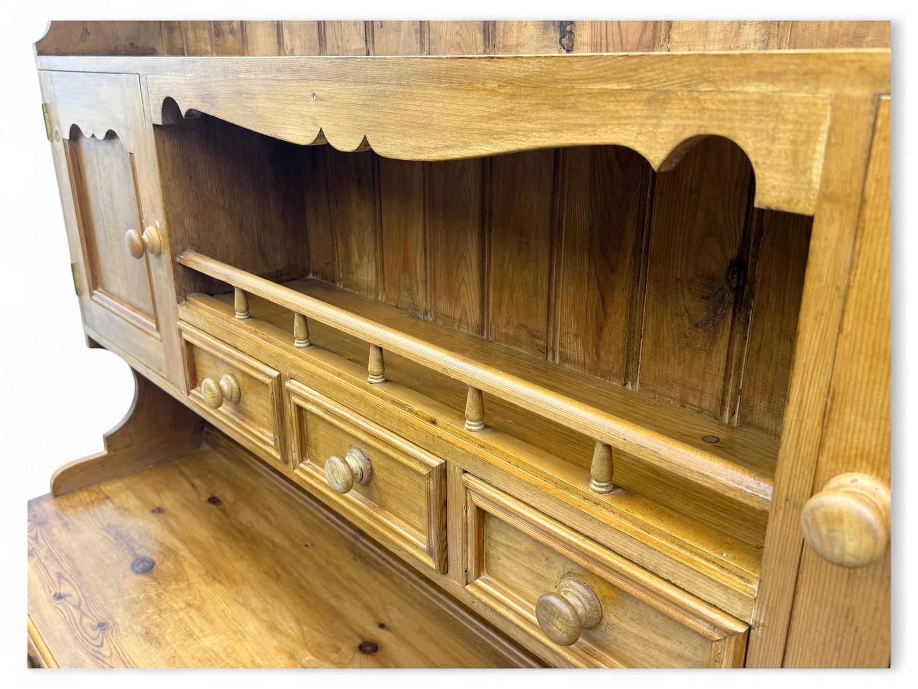Traditional vintage pine kitchen dresser with scrolled cornice and rack with long shelf above a galleried shelf flanked by three short drawers and two cupboards, the base with three long drawers above three cupboards on plinth base  