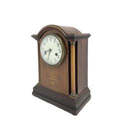 German - Edwardian 8-day mahogany mantle clock c1910, with a break arch pediment and two recessed columns with brass capitals, front decorated with an inlaid motif and satinwood stringing, on a stepped base with bun feet, white enamel dial with Arabic numerals, minute track and steel spade hands, two train countwheel striking movement striking the hours and half hours on a coiled gong. With pendulum & Key.