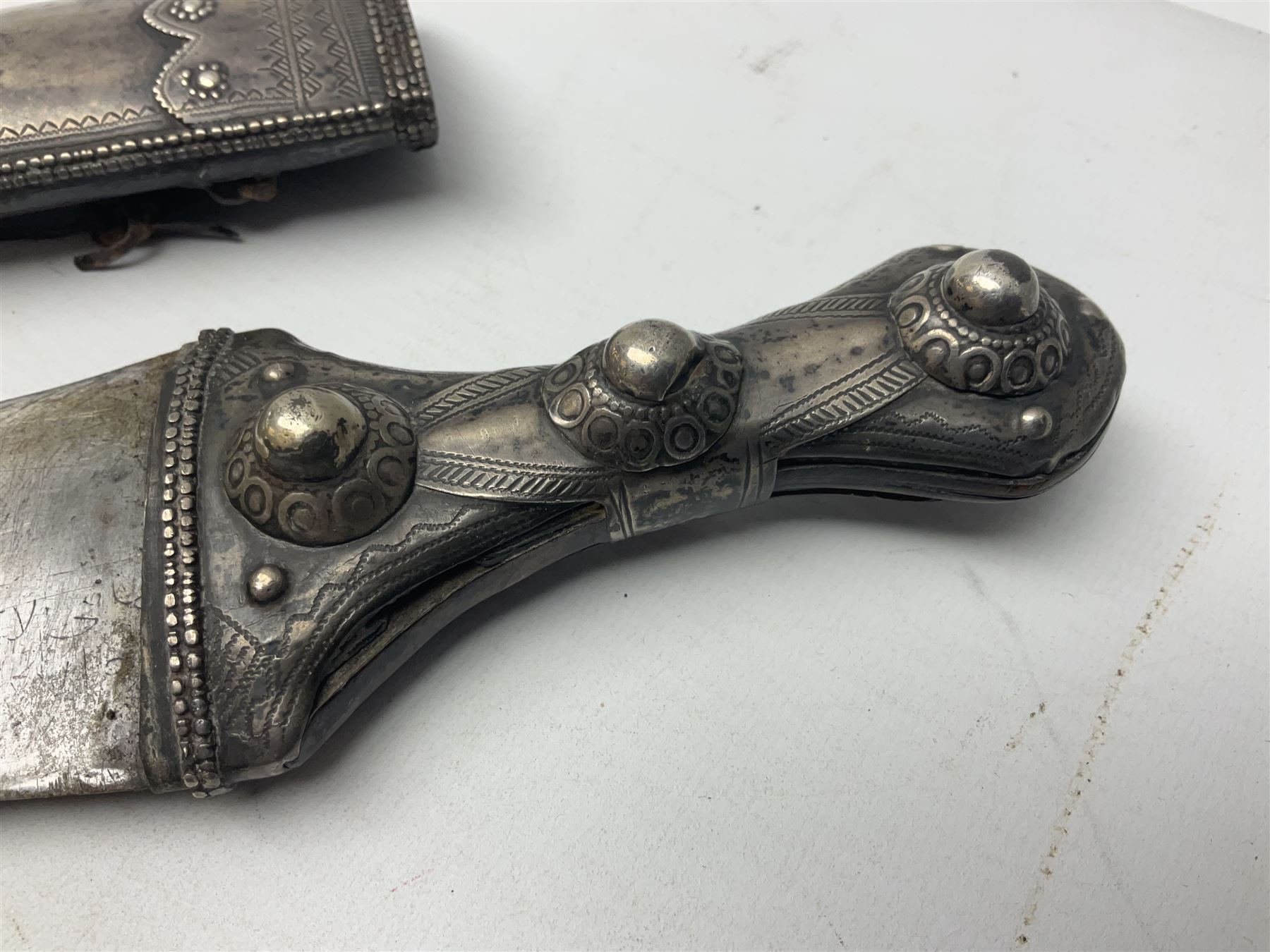Late 19th/20th century Middle Eastern jambiya dagger the 36cm broad curved double edged steel blade with traces of script, horn and copper backed waisted white metal hilt with three roundel buttons; in ornate white metal and leather mounted brass and steel scabbard L60.5cm overall