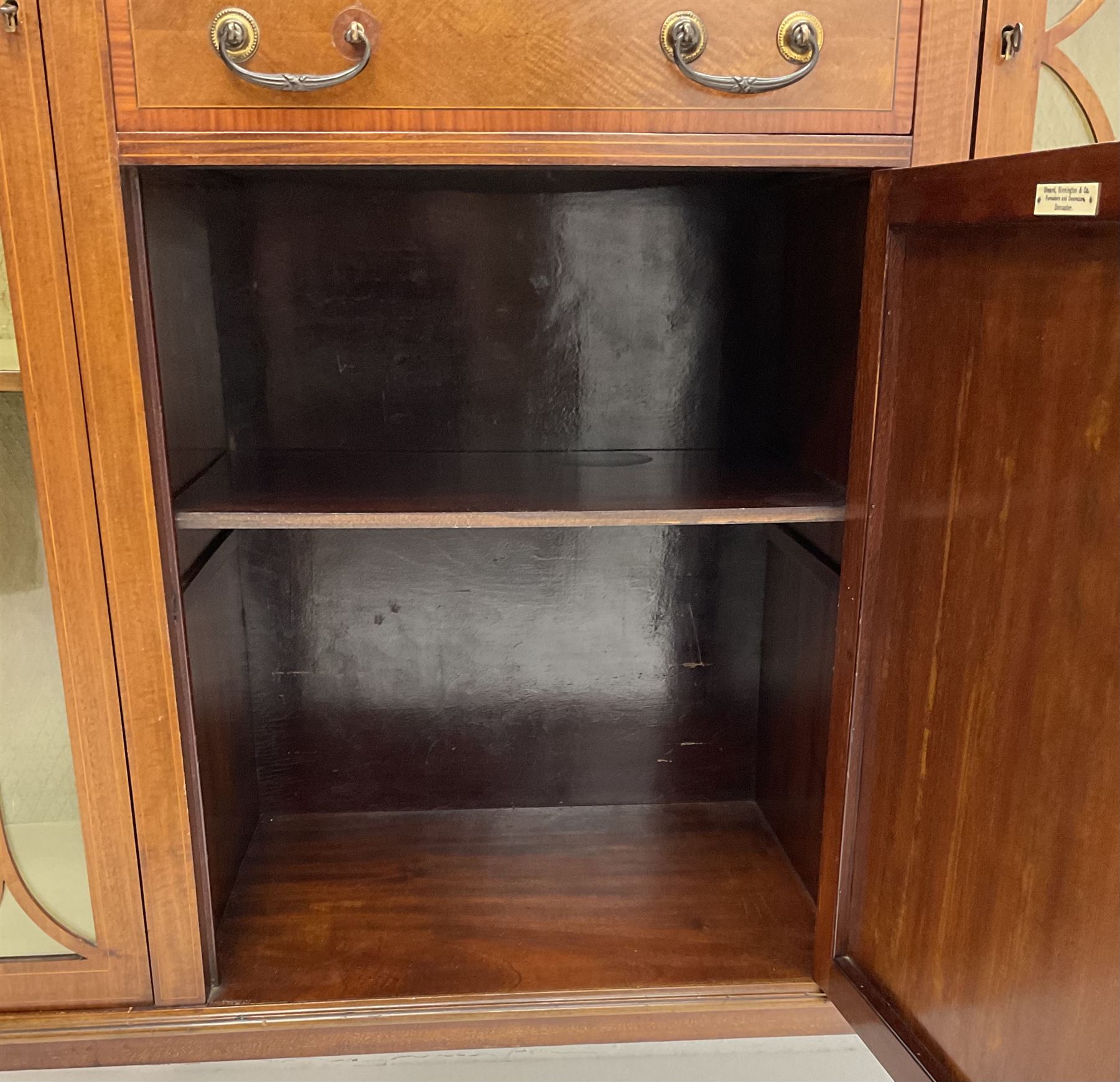 Edwardian inlaid mahogany display cabinet with ‘Shepard, Bennington & Co. Doncaster’ makers plaque, central bevel edge mirror flanked by two glazed doors enclosing two lined shelves, single drawer above cupboard on square tapering supports with spade feet