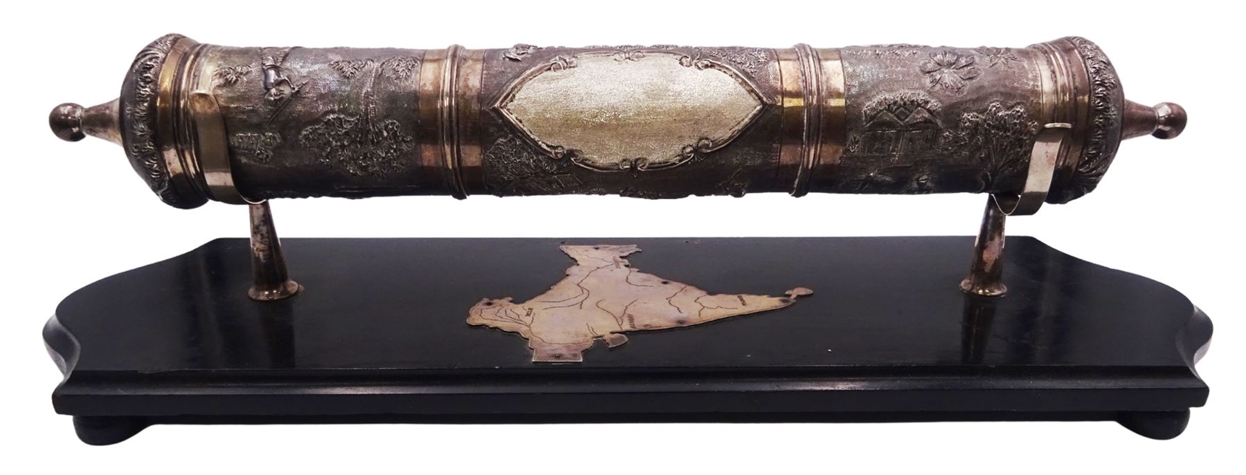 Late 19th/early 20th century Indian silver scroll holder, of cylindrical form with vacant cartouche and embossed with figures, animals and huts, upon a shaped ebonised stand with silver supports and silver panel of India