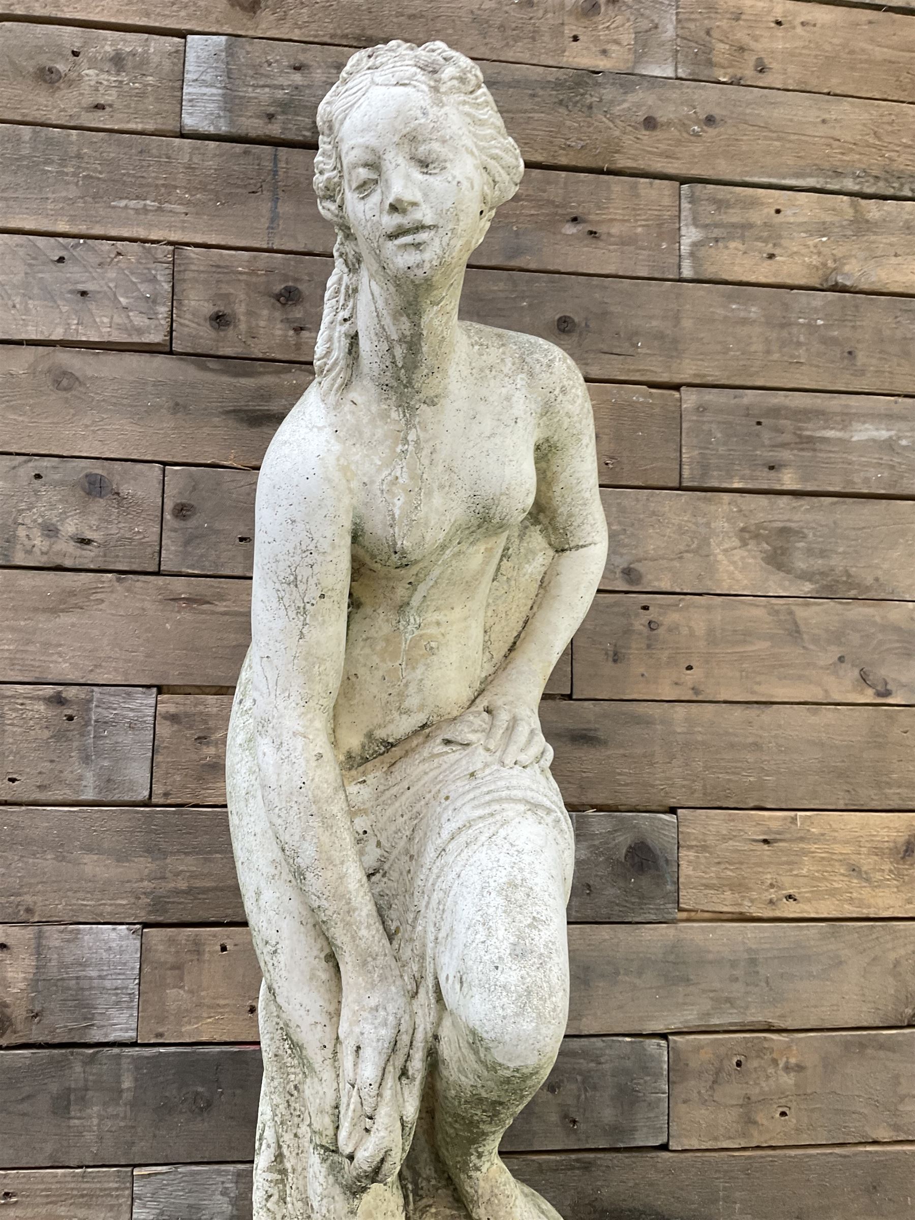 Cast stone garden statue of partially draped classical female figure on ornate pedestal 