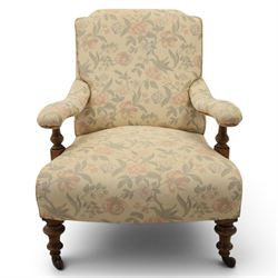 Victorian mahogany framed deep seat low drawing room chair, upholstered in beige floral fabric, on turned supports terminating in castors