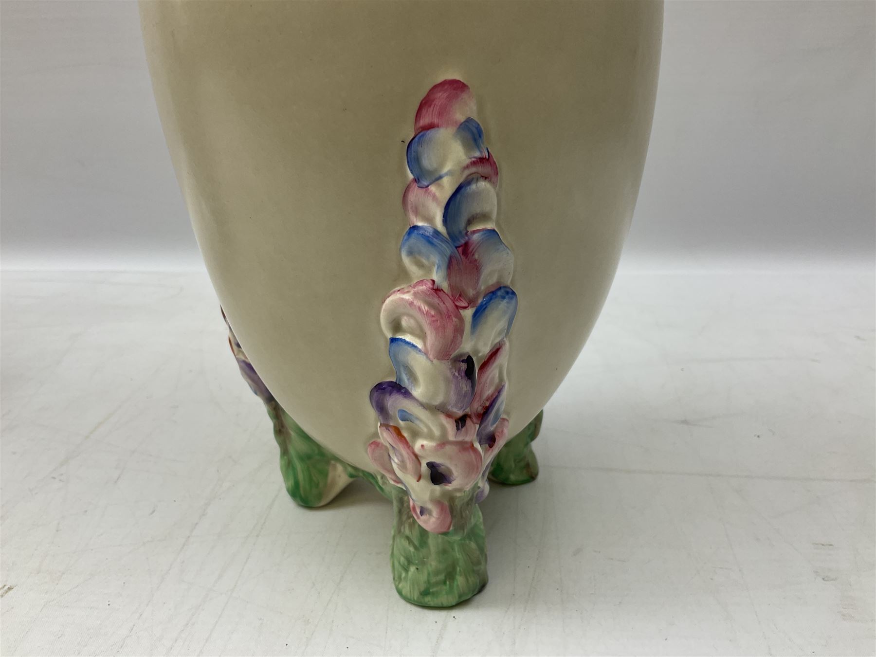 1930s Carlton Ware Art Deco Garden pattern vase of shouldered ovoid form, decorated with blue, pink and yellow flower heads on a mottled blue and white ground, pattern no. 3413, with printed and painted marks beneath, H19cm, together with a Clarice Cliff My Garden pattern vase, raised upon three feet with blue, pink and purple moulded Hollyhock design, H20cm, with Clarice Cliff Wilkinson Ltd England marks beneath