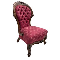 Victorian style mahogany framed nursing chair, the cresting rail carved with fruit and foliage, upholstered in red patterned fabric with buttoned back, on cabriole supports with scrolled terminals